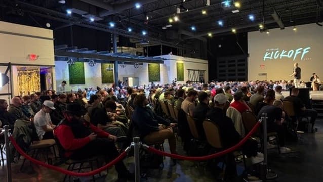 A packed event hall at a sales kickoff, with a speaker on stage