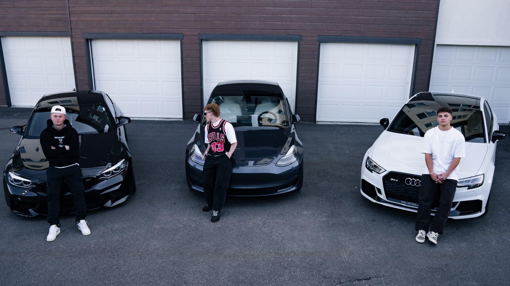 Three members of the CD Motion team standing with their cars in front of a row of garages