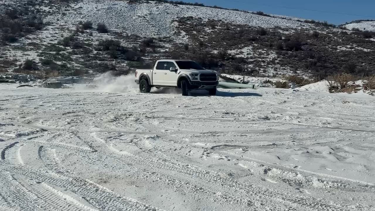 A white pickup truck kicking up snow on a hillside